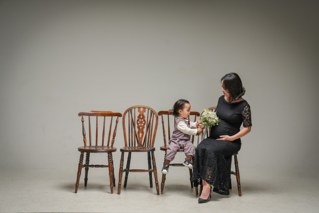 A happy Korean mother in her third trimester posing with her first child for a casual DIY maternity photoshoot at home, documenting her second pregnancy.